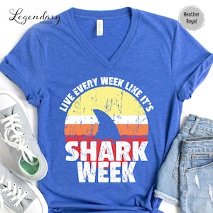 May include: A blue heather royal t-shirt with a vintage-style graphic of a shark fin and the text "Live Every Week Like It's Shark Week".