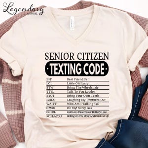a white t-shirt with a list of various texts and phrases, including "Best Friend Fell", "Little Old Lady", "Talk To You Louder", "Bring Your Own Teeth", "Laughing My Dentures Out", "OMG! Talking To You", "Gotta Go! Facemaker Battery Low", and "Rolling On The Floor And Can't Get Up".