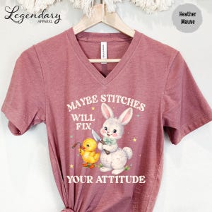 A pink t-shirt with a cartoon rabbit and a yellow duck, along with the text "MAYBE STITCHES WILL FIX YOUR ATTITUDE" printed on it.