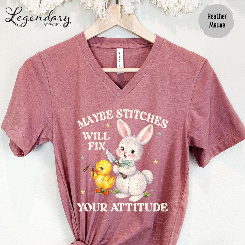 A pink t-shirt with a cartoon rabbit and a yellow duck, along with the text "MAYBE STITCHES WILL FIX YOUR ATTITUDE" printed on it.