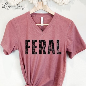 A pink t-shirt with the word "FERAL" printed in large, distressed font.