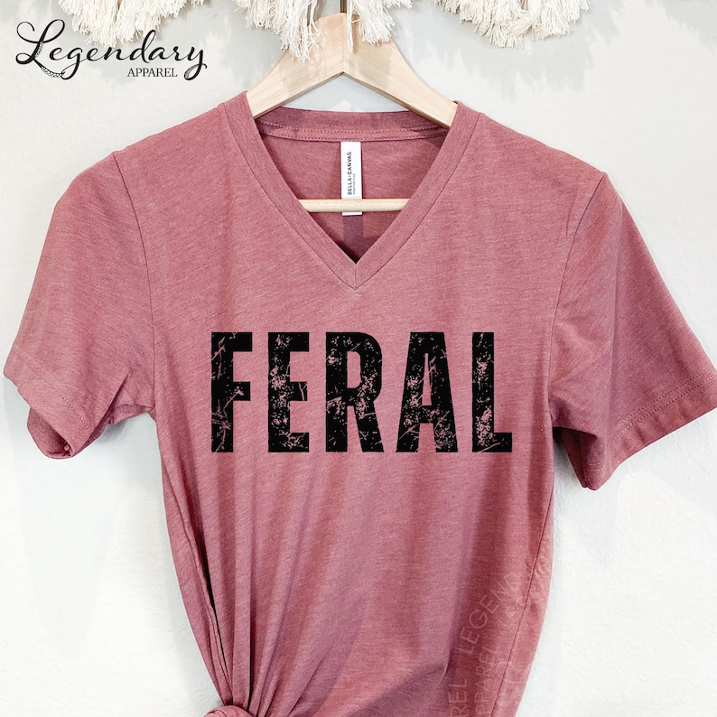 A pink t-shirt with the word "FERAL" printed in large, distressed font.