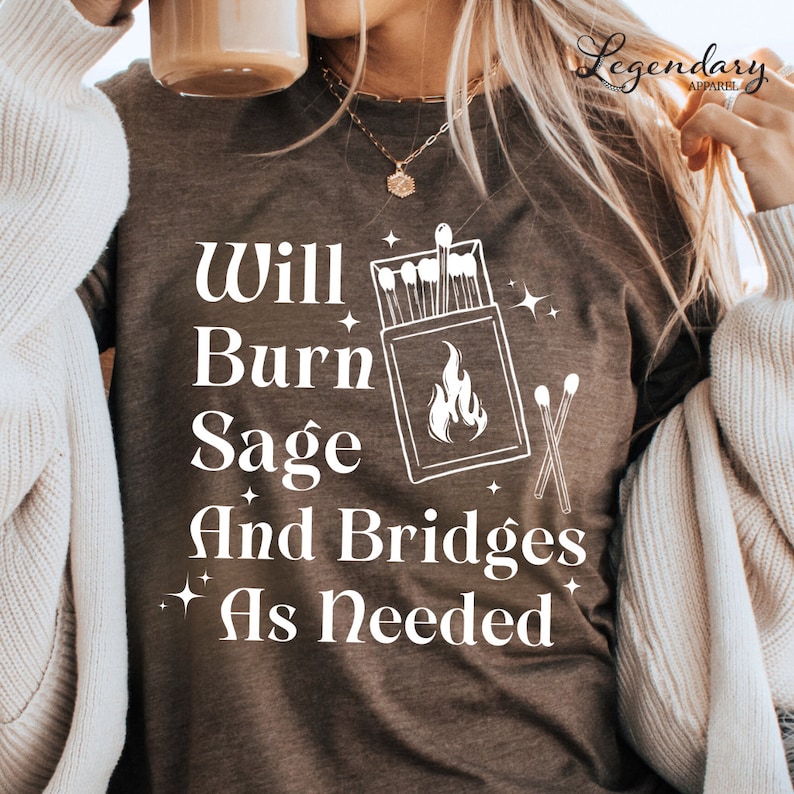 May include: A brown t-shirt with white text that reads "Will Burn Sage And Bridges As Needed". The text is accompanied by a graphic of a box of matches and a lit match.