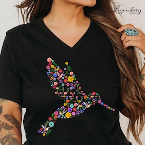 May include: Black v-neck t-shirt with a colorful hummingbird design made of flowers. The hummingbird is flying to the right and is outlined with flowers in shades of pink, purple, yellow, blue, and green.