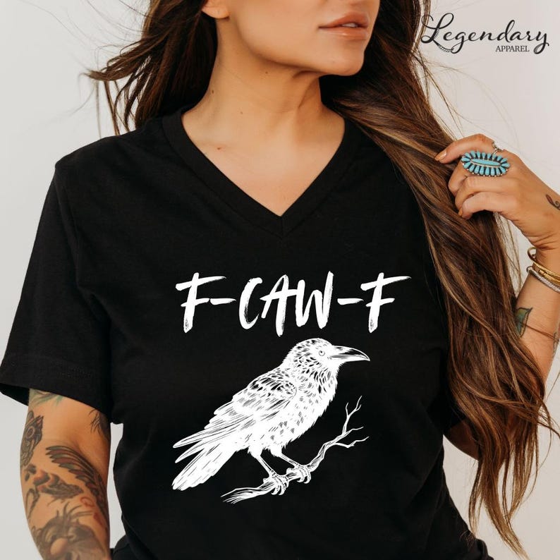 Pode incluir: T-shirt preta com decote em V com o texto branco "F-CAW-F" e uma ilustra&ccedil;&atilde;o detalhada de um corvo empoleirado num galho. A t-shirt &eacute; da Legendary Apparel.