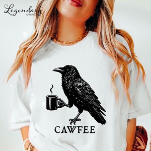 A woman wearing a white t-shirt with a black crow graphic and the text "CAWFREE" printed on it.