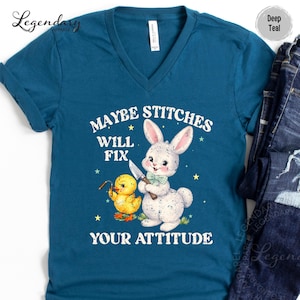 A blue t-shirt with a cartoon rabbit and a yellow duck holding a knife, along with the text "MAYBE STITCHS WILL FIX YOUR ATTITUDE".