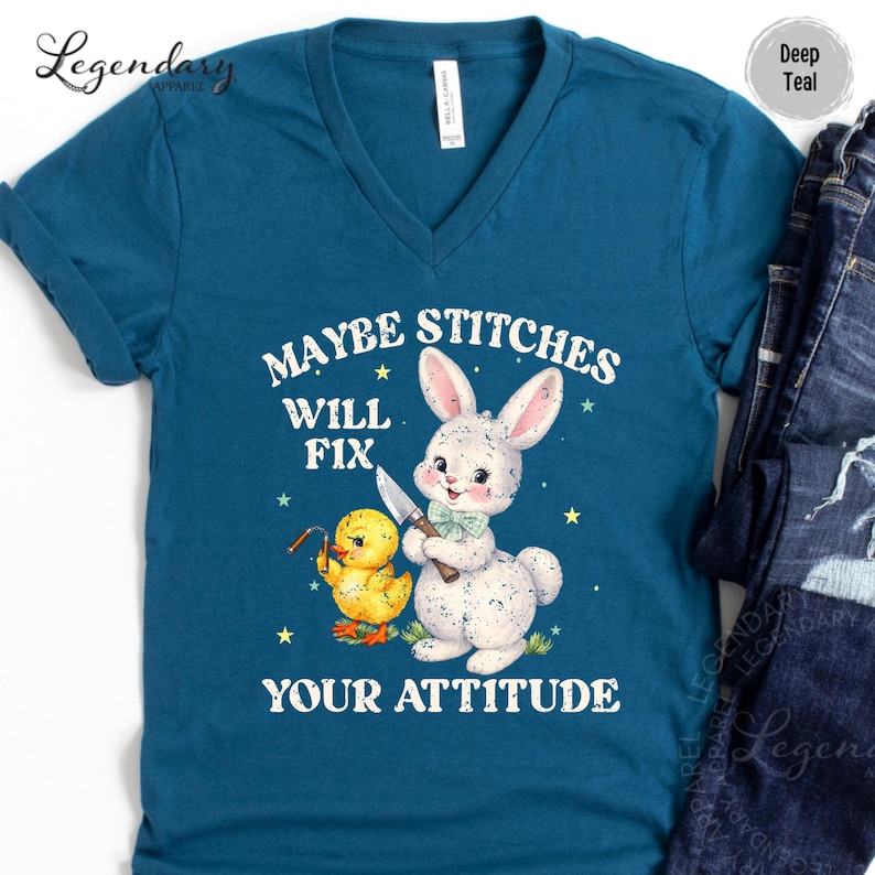 A blue t-shirt with a cartoon rabbit and a yellow duck holding a knife, along with the text "MAYBE STITCHS WILL FIX YOUR ATTITUDE".