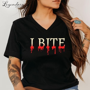 May include: Black V-neck t-shirt with the text "I BITE" in gold letters with red dripping blood effect. The shirt is from Legendary Apparel.