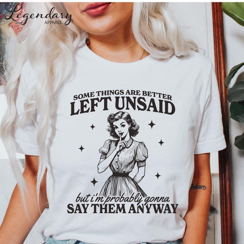 Może przedstawiać: Biała koszulka z napisem "SOME THINGS ARE BETTER LEFT UNSAID but I'm probably gonna SAY THEM ANYWAY." Grafika przedstawia ilustrację w stylu vintage kobiety z palcem na ustach, otoczoną gwiazdami.