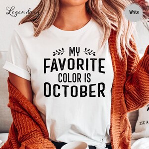 A person wearing a white t-shirt with the text "My favorite color is October" printed on it, along with a red sweater.