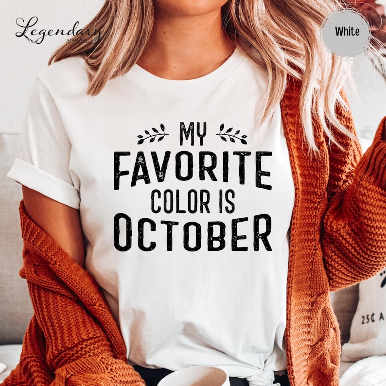 A person wearing a white t-shirt with the text "My favorite color is October" printed on it, along with a red sweater.