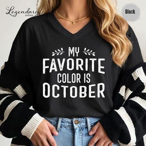 A person wearing a black and white striped sweater and a black t-shirt with white text that says "My favorite color is October".