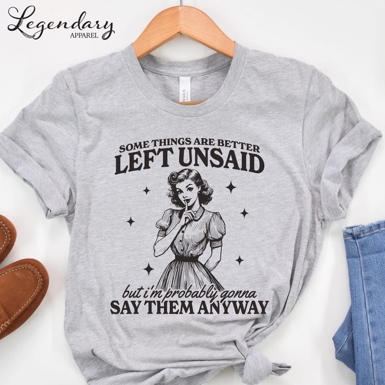 Może przedstawiać: Jasnoszara koszulka z napisem "SOME THINGS ARE BETTER LEFT UNSAID but I'm probably gonna SAY THEM ANYWAY." Koszulka przedstawia ilustrację w stylu vintage kobiety z palcem na ustach.