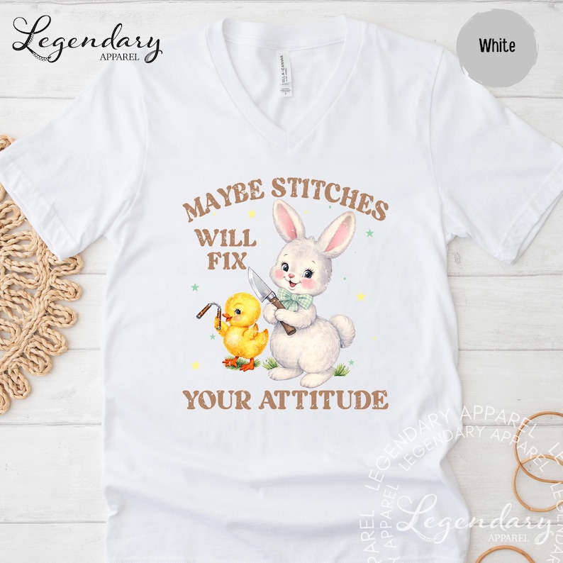 a white t-shirt with a graphic design depicting a rabbit and a duck, along with the text "MAYBE STITCHS WILL FIX YOUR ATTITUDE".