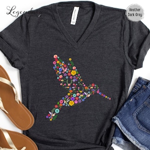 May include: Heather dark grey V-neck t-shirt with a floral hummingbird design. The hummingbird is made up of colorful flowers and leaves.