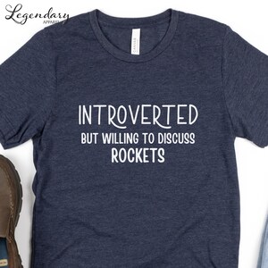 May include: A dark blue t-shirt with the text "Introverted but willing to discuss rockets" in white.
