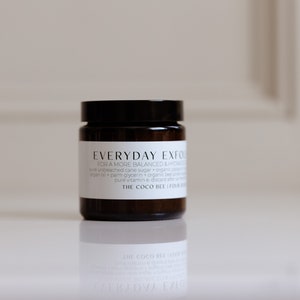 May include: A brown glass jar with a black lid containing a white label that reads "EVERYDAY EXFOLIATOR FOR A MORE BALANCED & HYDRATED SKIN" with the text "Pure unbleached cane sugar + organic bamboo + palm glycerin + organic base oils + pure vitamin E. Discard after four weeks." and the text "THE COCO BEE | FOUR OUNCES".