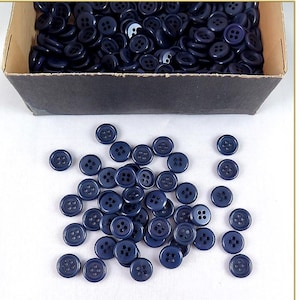 May include: A box of dark blue plastic buttons with four holes each. The buttons are in a cardboard box with a black interior.