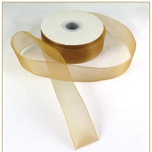 May include: A spool of gold-colored ribbon with a sheer, mesh-like texture. The ribbon is partially unrolled, revealing the spool's white core. The ribbon's color is a warm, metallic gold, suitable for gift wrapping or crafting.