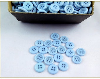 May include: A box of light blue plastic buttons with four holes each. The buttons are scattered on a white surface.