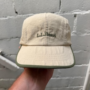Op de afbeelding: Een baseballpet met vijf panelen in een lichtbeige kleur met een donker olijfgroene bies langs de rand van de klep. De tekst L.L.Bean is in donker olijfgroene draad geborduurd op het midden van de voorzijde, met zichtbare stiksels.