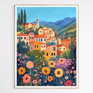 May include: A framed art print depicting a vibrant Italian village scene. The artwork features colorful buildings with red tile roofs, a blue-domed structure, and lush floral foreground with sunflowers, all under a clear blue sky.