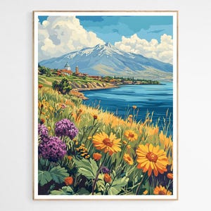 May include: A framed art print of a coastal landscape. The artwork depicts a mountain range, a body of water, and a village. The foreground features wildflowers in shades of yellow, orange, and purple. The sky is blue with white clouds.