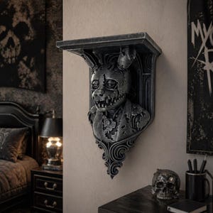 Op de afbeelding: Donkergrijze wandplank met een gestileerde buste van een konijnachtig figuur met een verweerde, metalen afwerking. De plank heeft een decoratieve beugel en is bevestigd aan een neutraal gekleurde muur. Het thema is gotisch en macaber.
