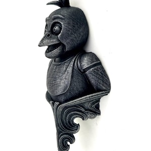 Pode incluir: Escultura detalhada, com aspeto metálico, de uma criatura semelhante a um pássaro com bico aberto e crista. A escultura tem um acabamento texturizado e é montada numa base decorativa em forma de voluta. O pássaro usa um colete.