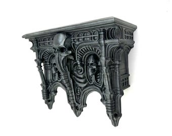 Puede incluir: Una estantería de pared de color gris oscuro, de estilo gótico, con intrincados detalles esculpidos. La estantería presenta una calavera y elementos biomecánicos, con una superficie texturizada y un diseño arquitectónico complejo. La estantería está montada sobre un fondo blanco.