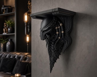 Op de afbeelding: Een matzwarte wandplank met een sculpturale alien-kop als steunbeugel. Het ontwerp bevat gedetailleerde dreadlock-achtige elementen met gouden metalen ringen en een textuurrijke, organische vorm die naar beneden toe uitloopt.