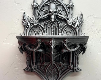 Puede incluir: Estantería de pared de estilo gótico en tonos grises, con intrincados detalles arquitectónicos. El diseño incluye una calavera, elementos arqueados y una balda. La estantería está montada en una pared texturizada.