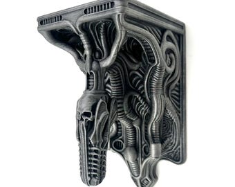 May include: A silver-colored, wall-mounted shelf bracket with an intricate, biomechanical design. The bracket features a skull-like element and a complex network of organic-looking tubes and structures, creating a unique, industrial aesthetic. The shelf is designed to be mounted on a wall.