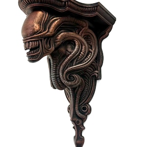Puede incluir: Una estantería de pared de color bronce con un diseño detallado y esculpido de una criatura alienígena. La estantería tiene una parte superior decorativa y una parte inferior puntiaguda, con texturas intrincadas y orgánicas.