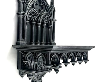Puede incluir: Una estantería de pared de estilo gótico gris oscuro con intrincados detalles arquitectónicos. La estantería presenta un diseño de arco apuntado, columnas y elementos decorativos, creando una estética medieval. La estantería está montada en una pared blanca.