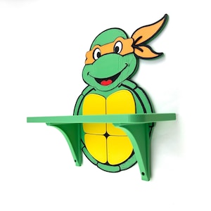May include: A green shelf shaped like a cartoon turtle character, featuring a yellow shell and orange mask. The shelf is mounted on a white wall, offering a playful storage solution for a child's room or themed space.