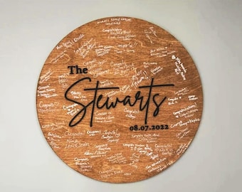 May include: A round wooden sign with the text "The Stewarts" and the date "08.07.2022" written in black. The sign is covered in white signatures and well wishes.