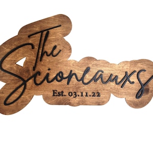 May include: A wooden sign with the text "The Scioneauxs Est. 03.11.22" in black script font.