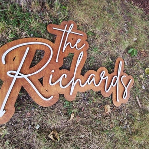 Pode incluir: Uma placa de madeira com as palavras "The Richards" em letras brancas em cursiva. A placa &eacute; marrom e tem um visual r&uacute;stico.