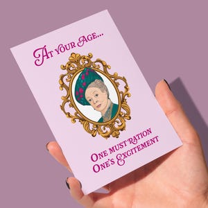 May include: A rectangular greeting card with a light purple background featuring a gold ornate oval frame containing an illustration of an older person wearing a teal hat with pink flowers. The text reads At your age... One must ration one's excitement.