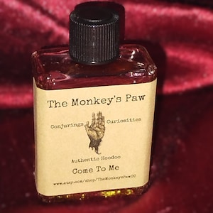 Può includere: Una piccola bottiglia di vetro con un tappo nero e un'etichetta marrone. L'etichetta recita "The Monkey's Paw Conjuring Curiosities Authentic Hoodoo Come To Me www.etsy.com/shop/TheMonkeysPawCO"