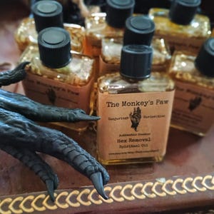 May include: Multiple small glass bottles filled with a golden liquid. The bottles are labeled "The Monkey's Paw" and "Hex Removal Spiritual Oil".