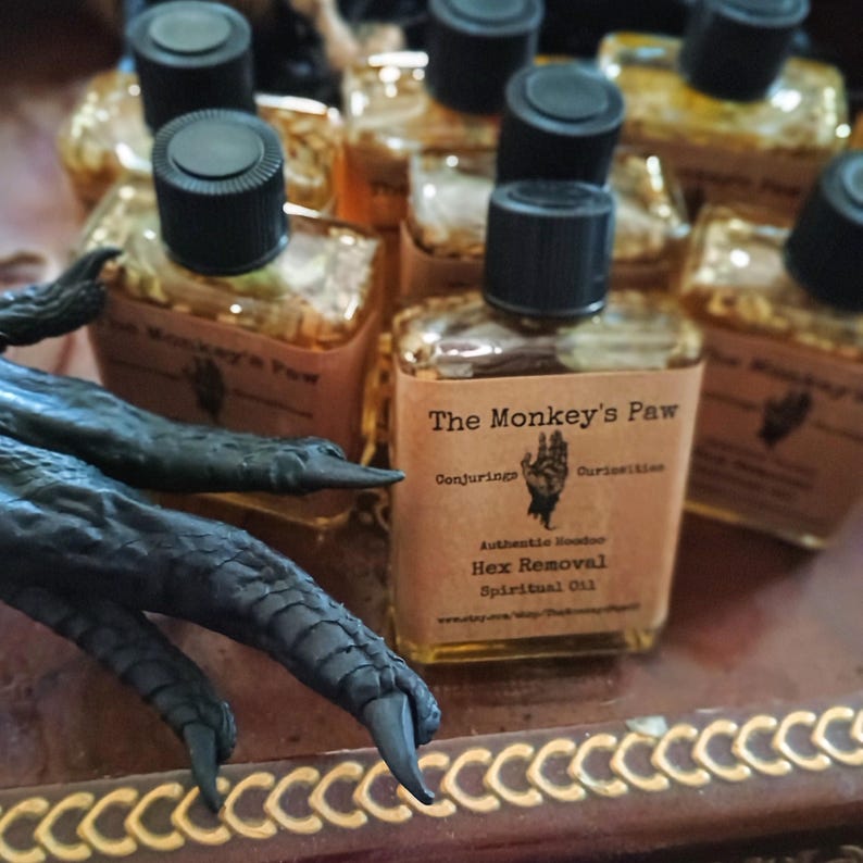 May include: Multiple small glass bottles filled with a golden liquid. The bottles are labeled "The Monkey's Paw" and "Hex Removal Spiritual Oil".