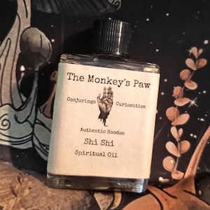 May include: A small glass bottle with a black cap, labeled "The Monkey's Paw Conjuring's Curiosities Authentic Hoodoo Shi Shi Spiritual Oil".
