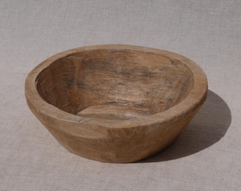 May include: A handcrafted wooden bowl with a natural, light brown finish. The bowl has a rounded shape with a slightly irregular rim, showcasing the wood grain. The interior is smooth, while the exterior has a textured appearance.