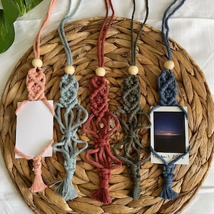 May include: Five macrame keychains with wooden beads and tassels. The keychains are in different colors: pink, blue, red, green, and dark blue. Each keychain has a small card attached to it, one of which has the text "Topsail 2022".