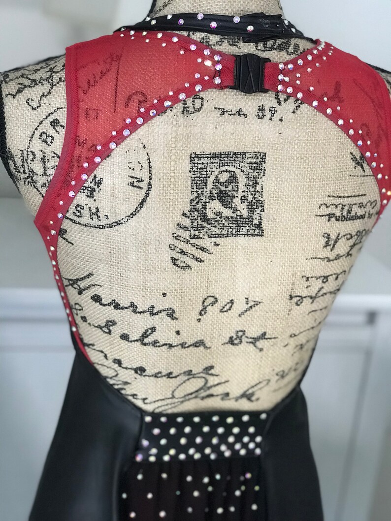 May include: Black and red dance costume with a mesh back and rhinestones. The costume has a halter neckline and a fitted bodice.