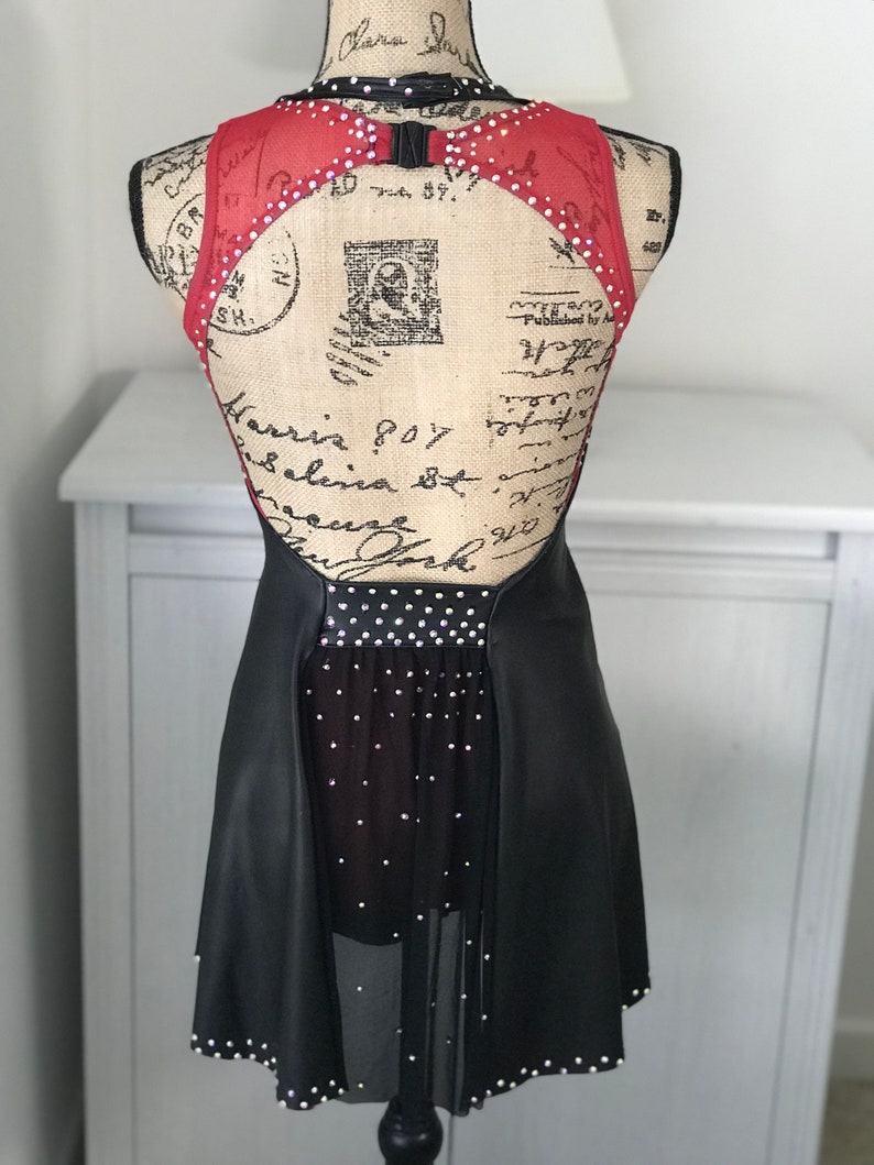 May include: Black and red dance costume with a sheer skirt and rhinestones. The costume has a low back with a cutout and a black belt.