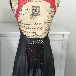 May include: Black and red figure skating dress with a mesh skirt and rhinestones. The dress has a low back and a scoop neckline.
